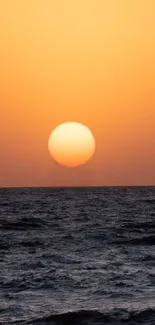 Serene sunset over ocean with orange sky and dark waves.