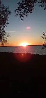 Serene sunset over a lake with silhouetted trees and vibrant sky.