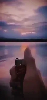 Hand holding lighter against a beautiful sunset over a lake.