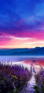 Vibrant sunset over a lake with mountains and purple flowers.