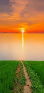 Scenic sunset over a calm lake with vibrant orange hues and green fields.