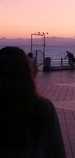 A serene sunset with pink and purple tones over the ocean and boardwalk.