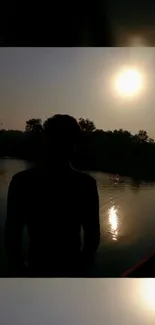 Silhouette of a person by a lake at sunset.