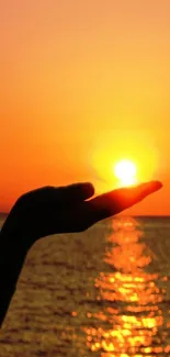 Silhouette of a hand holding the sun against an orange ocean sunset.