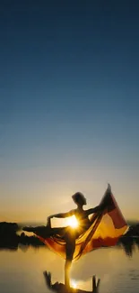 Silhouette dancing at sunset over tranquil water.