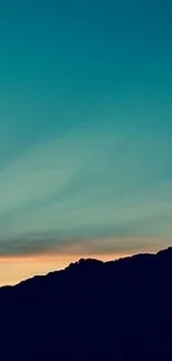 Teal sky and dark mountain silhouette at sunset.