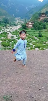 Child in blue traditional attire in a tranquil village landscape with green hills.