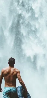 Man with tire facing majestic waterfall.