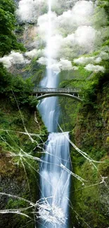 Breathtaking waterfall amidst lush greenery with a small footbridge.