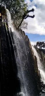 Serene waterfall with blue sky and rock formations, perfect for phone wallpaper.