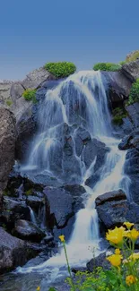 Cascading waterfall with blue sky and flowers in nature scene.