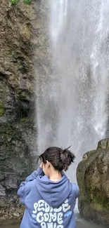 A person stands before a cascading waterfall.