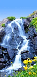 Serene waterfall with wildflowers and rocky cliffs under a blue sky.