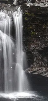 Serene waterfall with dark rocks and lush green foliage.