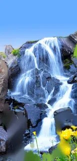 A serene waterfall with vibrant yellow flowers and lush greenery under a clear sky.