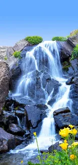 Peaceful waterfall with blue sky and vibrant flora, ideal for a mobile wallpaper.