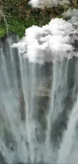 Tranquil waterfall with lush greenery and misty clouds.