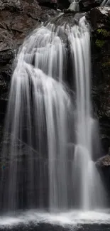 Peaceful waterfall amidst rocky cliffs and greenery.