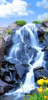 Beautiful waterfall with bright blue sky and yellow flowers in a serene setting.