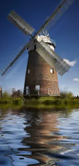 Scenic view of a windmill by a reflective lake under a bright blue sky.