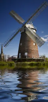 Windmill reflection on water with clear blue sky.