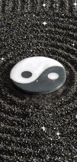 Yin Yang symbol on textured black sand with sparkling accents.