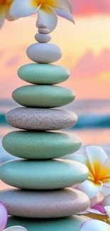 Stacked Zen stones on a serene beach at sunset with flowers.