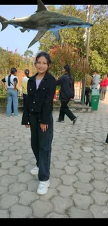 Girl in a park with a shark overhead.