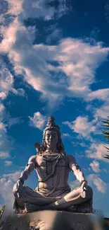 Serene Shiva sculpture under vibrant blue sky with clouds.