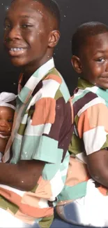 Smiling siblings in colorful shirts with a baby on a dark background.