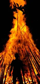 Silhouette standing against a towering bonfire with bright orange flames.