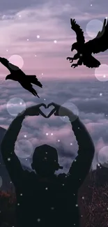 Silhouette forming heart with hands beneath eagles against pink sky.