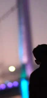 Silhouette against a colorful, illuminated bridge at night.