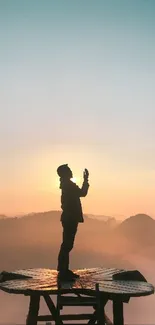 Silhouette on platform against sunrise over mountains.