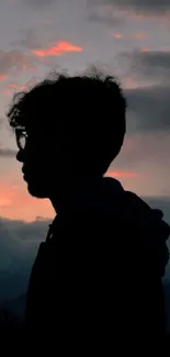 Silhouette of person against dramatic sunset sky with clouds.