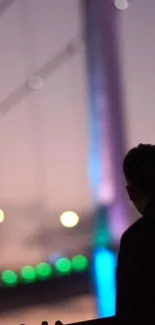 Silhouette of person with colorful bridge in the background at dusk.