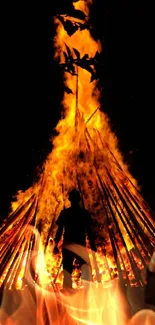 Silhouette of person by large bonfire at night.