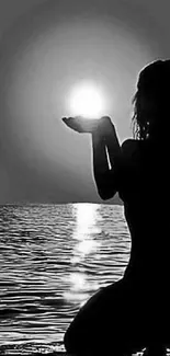 Silhouette of a person holding the sun by the ocean.