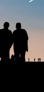 Silhouette of a couple walking against a blue to peach sunset sky.