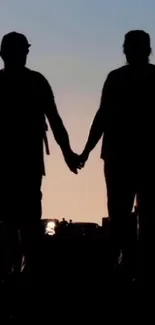 Silhouette of couple holding hands at sunset.