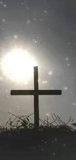 Silhouette of cross at sunset with radiant sun and dark landscape.