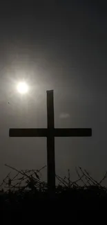 Silhouette of a cross against a setting sun and dark sky.