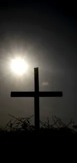 Silhouette of a cross against a sunset sky with bright sun rays.