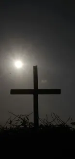 Dark silhouette of a cross against a sunset sky for mobile wallpaper.