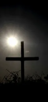 Silhouette of a cross against a sunset sky with a glowing sun.