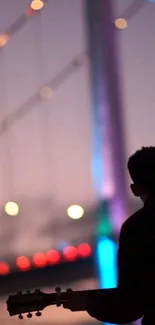 Silhouetted guitarist with a colorful bridge in background at twilight.