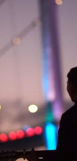 Silhouette of guitarist against colorful evening bridge lights.