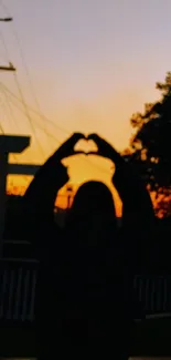 Silhouette of a person making a heart shape against a sunset background.