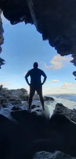 Silhouette of person in rocky ocean cave with blue sky.