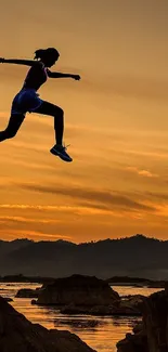 Silhouette of person jumping over rocks at sunset.